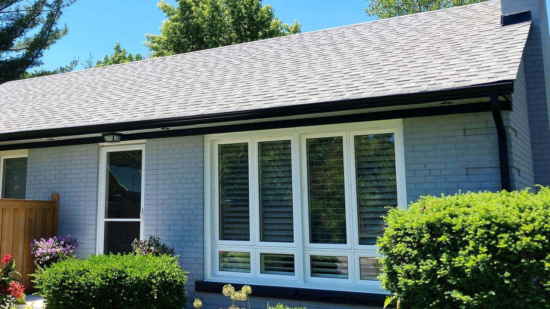 The front of a blue brick house featuring the Peak gutter system in black installed along the exterior.